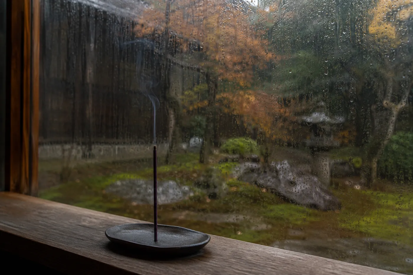 雨粒の伝う窓辺で、香立てに立てたお香から細く煙が上がっている様子